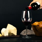 photo of person pouring wine into glass besides some cheese