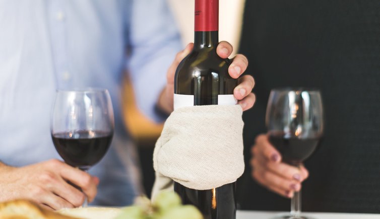 man holding white labeled red wine bottle near wine glasses